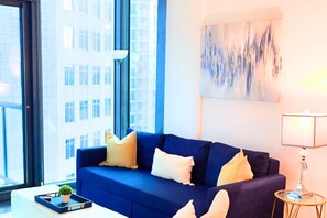 A modern living room with a blue sofa, a small table with a plant, and a lamp. - The Luxe | City View | Romantic Escape (Atlanta)