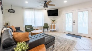 Un salon moderne avec un canapé en cuir noir, une petite table basse ronde, un fauteuil vert et un téléviseur fixé au mur.