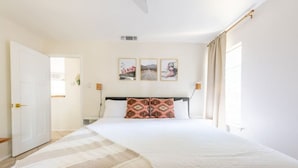 Une chambre à coucher avec un grand lit, une porte, une table de chevet et des œuvres d’art murales.