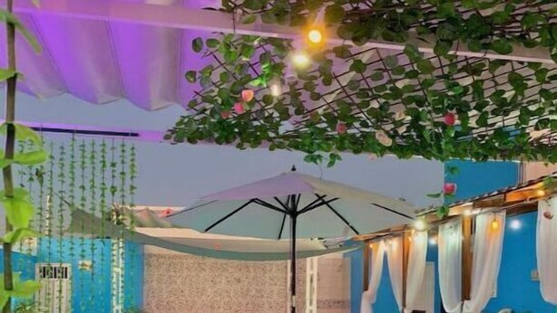 Un espace extérieur aménagé avec des chaises et une table en bois, une piscine et un coin salon couvert agrémenté de rideaux.