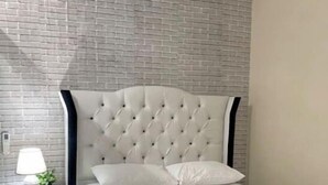 Une chambre à coucher avec une tête de lit capitonnée, une table de chevet avec une lampe et une petite plante.