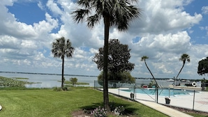 A pool area with a fence, palm trees, and a view of a body of water. - 2 Bed/2 Bath Condo - Close to Downtown Sebring & Racetrack (Sebring)
