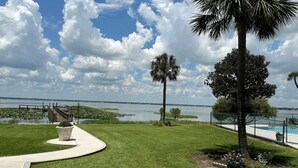 A well-maintained grassy area with a pathway leading to a dock over water, surrounded by palm trees and a fenced swimming pool. - 2 Bed/2 Bath Condo - Close to Downtown Sebring & Racetrack (Sebring)