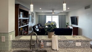 A modern living room with a kitchen area, a ceiling fan, a TV mounted on the wall, and a potted plant. - 2 Bed/2 Bath Condo - Close to Downtown Sebring & Racetrack (Sebring)