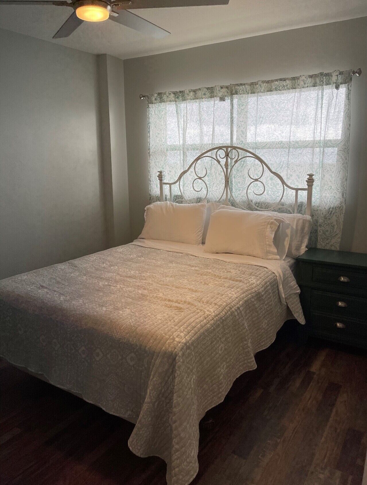 A bedroom with a bed, a nightstand, a ceiling fan, and a window with curtains.