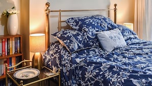 A neatly arranged bedroom with a bed, bedside table, lamp, and a bookshelf.