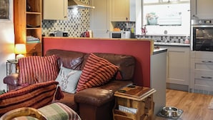 A cozy living room with a brown leather sofa, a wooden side table, and a kitchen area with modern appliances.