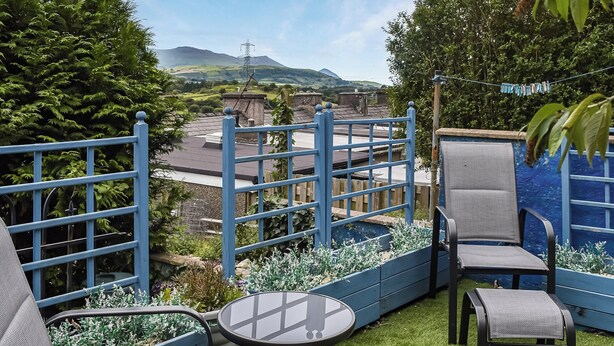 A patio with outdoor seating, a small table, and a view of a mountainous landscape.