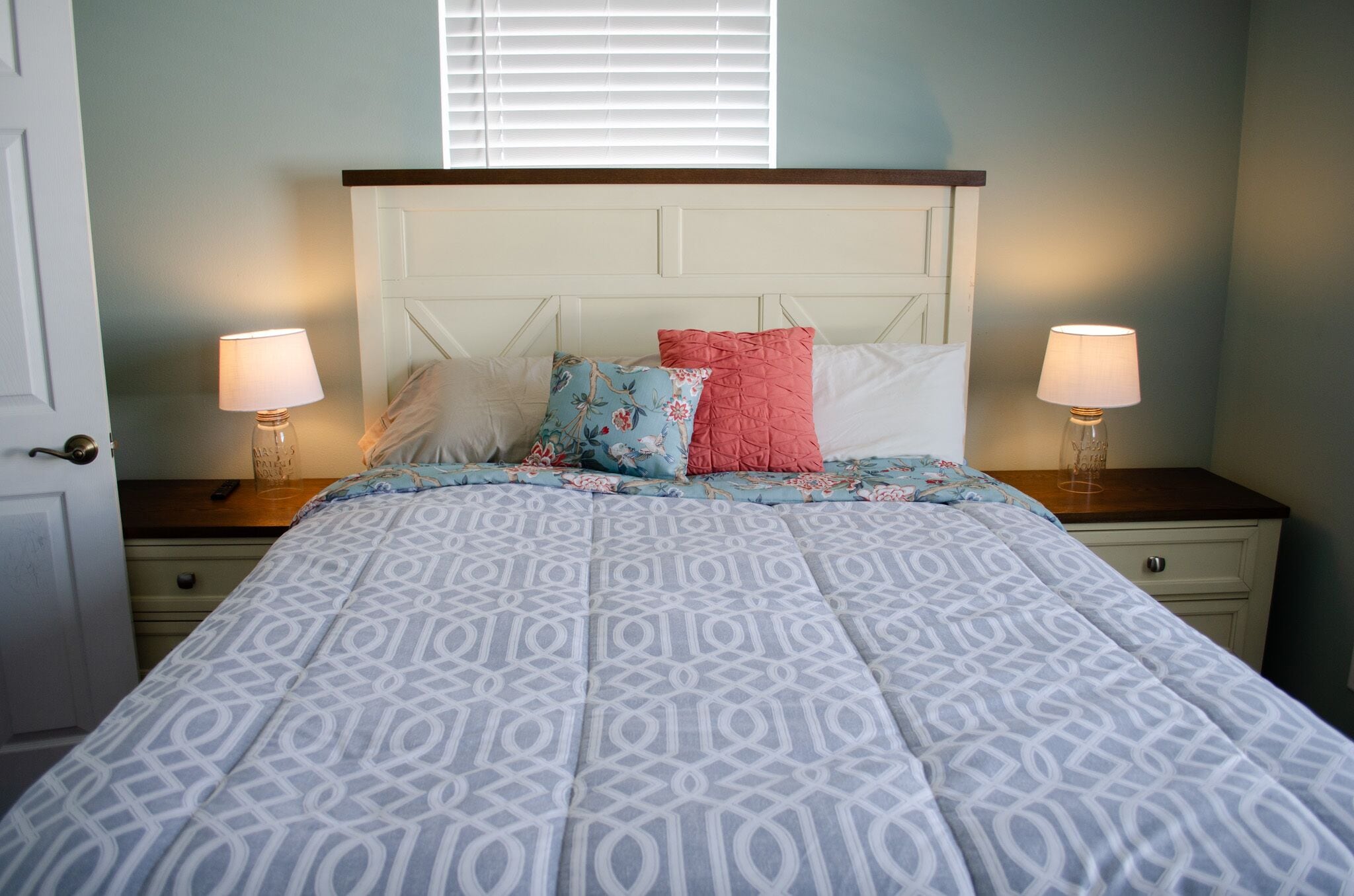 Une chambre à coucher avec une couvre-lit à motifs, deux lampes de chevet et une fenêtre avec des stores.