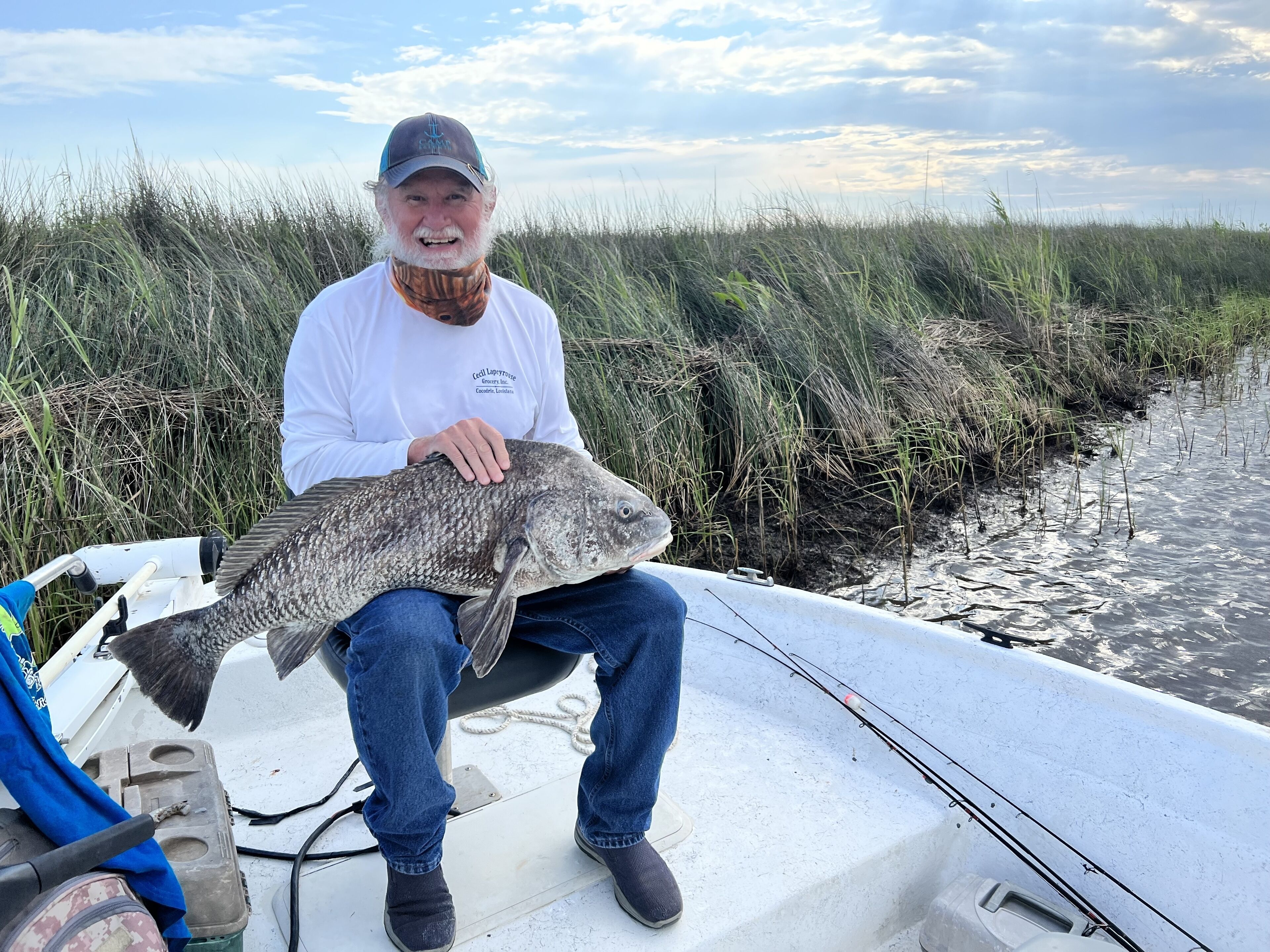 En person håller i en stor fisk på en båt, med en grönskande strand i bakgrunden.