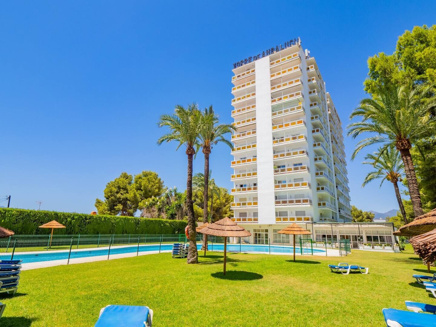 Ein Hochhaus-Hotel mit Swimmingpool und Liegestühlen.