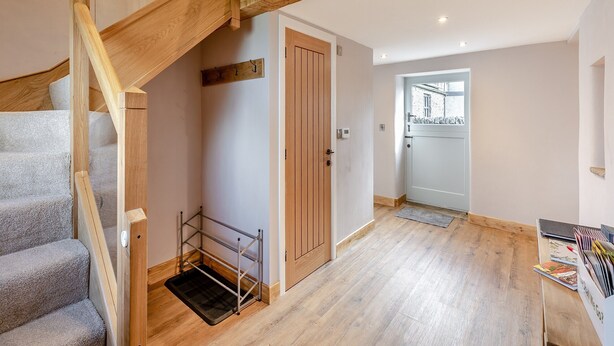 A spacious hallway with a wooden staircase, a door with a coat rack, and a view into another room.