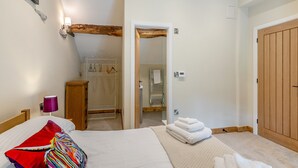 A bedroom with a bed, a wooden wardrobe, a coat rack, and a bathroom visible through an open door.