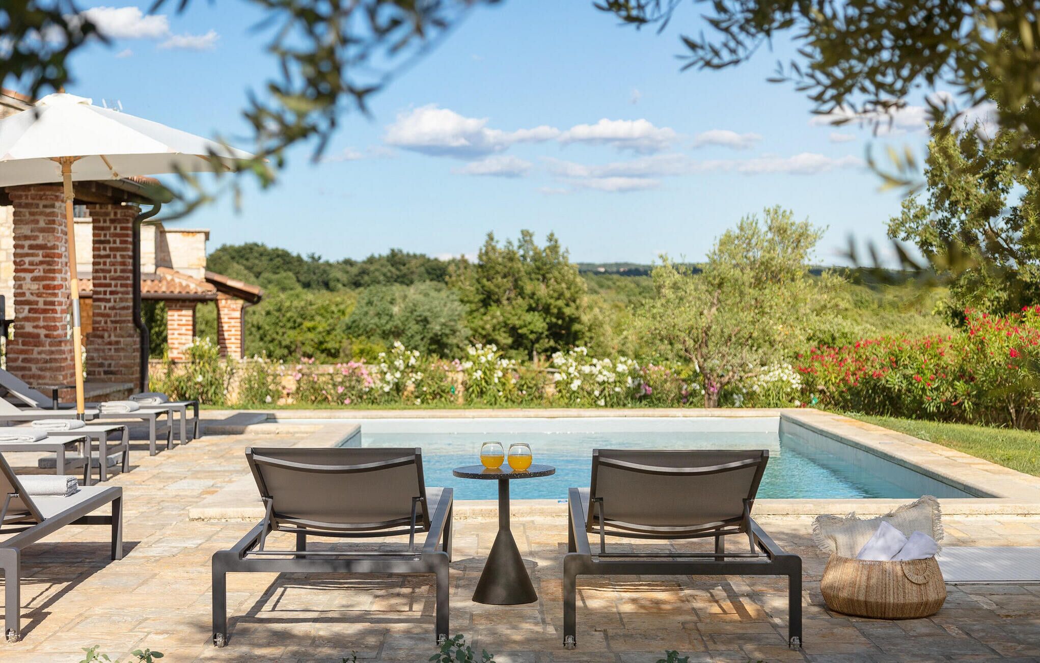 A poolside area with lounge chairs, a table with drinks, and a view of the pool and surrounding greenery.