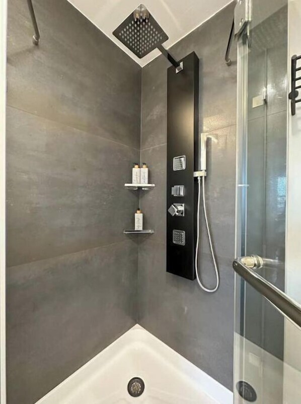 Un espace douche moderne doté d’une paroi en verre, d’un pommeau de douche à main et d’un panneau de commande.