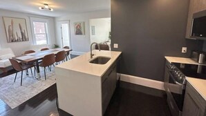 A modern kitchen with a central island, dark walls, and a dining area with a table and chairs. - Chic Downtown Salem 3 Bedroom w/ Parking (Salem)