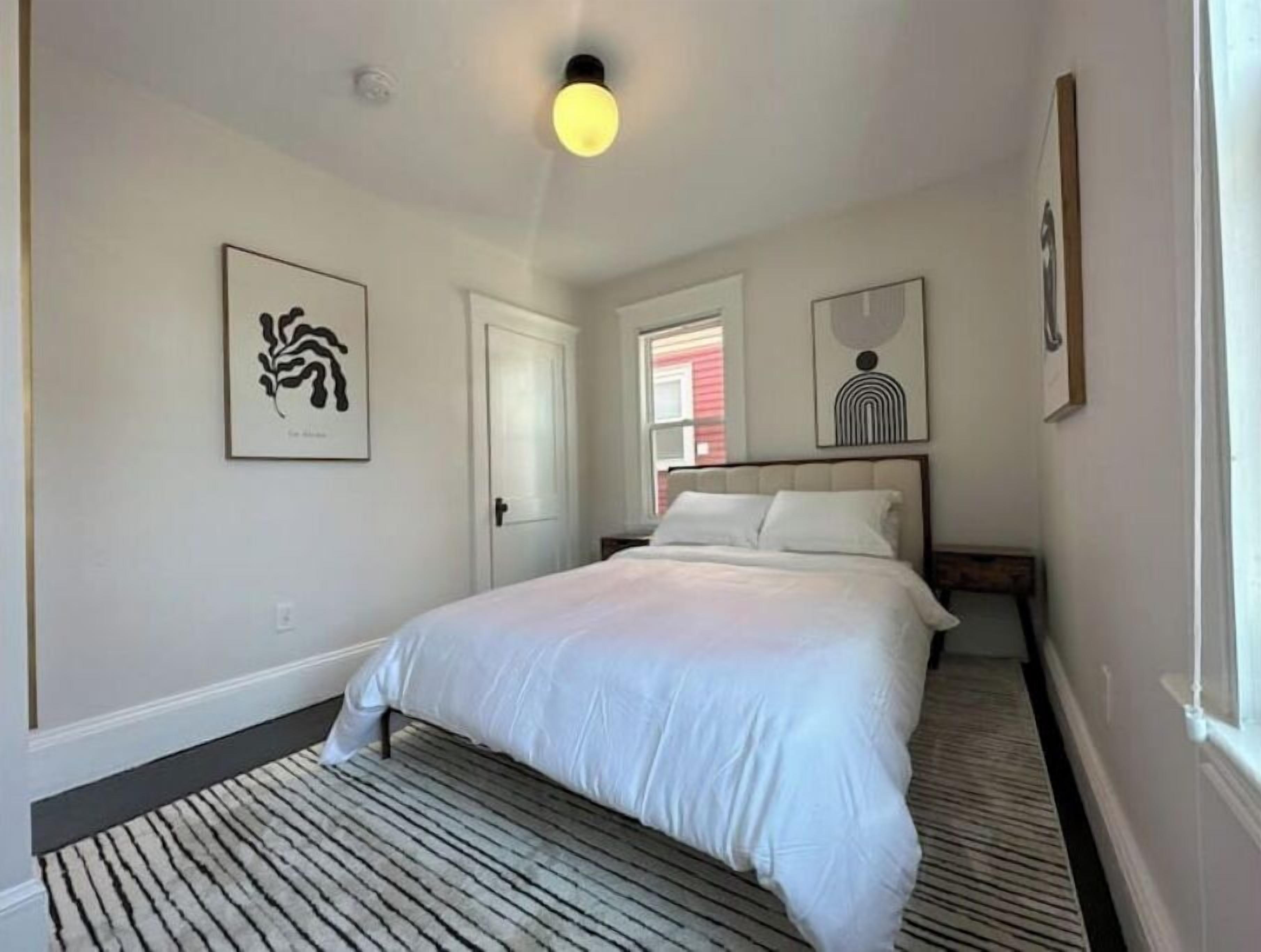 Une chambre à coucher avec un lit, une fenêtre et des œuvres d’art accrochées aux murs.