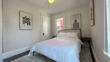 Une chambre à coucher avec un lit, une fenêtre et des œuvres d’art accrochées aux murs.