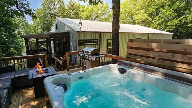 A hot tub with a wooden deck and outdoor seating area, a barbecue grill, and a small shed. - Hot Tub in the Woods, Fire Pit, Pet Friendly (Eureka Springs)