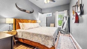 A bedroom with a wooden bed, a ceiling fan, and guitars on the wall. - Hot Tub in the Woods, Fire Pit, Pet Friendly (Eureka Springs)