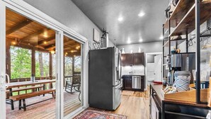 A kitchen with a large refrigerator, wooden cabinets, and a dining area with a bench and table. - Hot Tub in the Woods, Fire Pit, Pet Friendly (Eureka Springs)