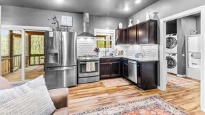A modern kitchen with stainless steel appliances, dark cabinetry, and a wooden floor. - Hot Tub in the Woods, Fire Pit, Pet Friendly (Eureka Springs)