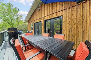 Une terrasse avec une table en bois et des chaises orange, un barbecue et un parasol bleu.
