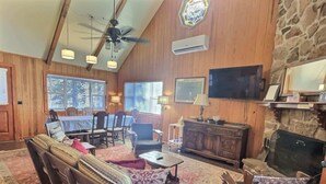 A cozy living room with wooden walls, a stone fireplace, a ceiling fan, and a flat-screen TV. - Lake Front | Fire Pit | Kayaks | Classic LakeCabin (Eureka Springs)