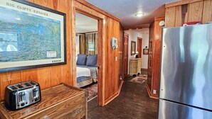 A compact kitchen with wooden cabinets, a stainless steel refrigerator, a toaster, and a framed map on the wall. - Lake Front | Fire Pit | Kayaks | Classic LakeCabin (Eureka Springs)
