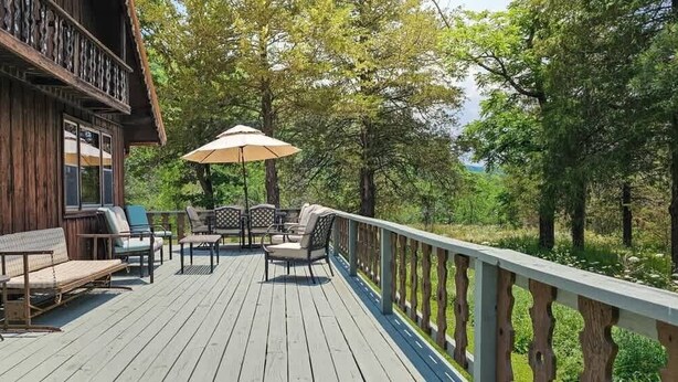 A wooden deck with outdoor furniture, including a table and chairs, and a large umbrella. - Lake Front | Fire Pit | Kayaks | Classic LakeCabin (Eureka Springs)