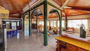 A spacious interior with a high ceiling, wooden beams, and a central open area with a staircase. - Oceanfront Oasis with Meditation Tower & Pool (Hopeville)