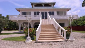 A large, two-story house with a balcony, a staircase, and a well-maintained garden. - Oceanfront Oasis with Meditation Tower & Pool (Hopeville)