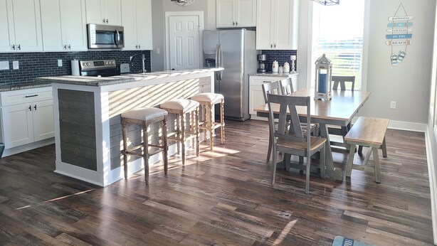 A modern kitchen with white cabinets, a central island with stools, stainless steel appliances, and a dining area with a wooden table and chairs.