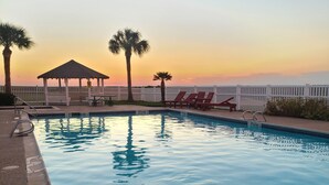 A swimming pool with lounge chairs and a gazebo, surrounded by a white fence and palm trees.