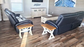 A living room with a black leather sofa, two wooden side tables, a white cabinet, and a television mounted on the wall.