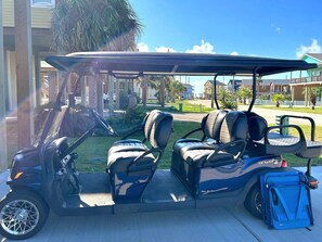 A golf cart parked in a residential area with a covered seating area and a blue storage box attached.