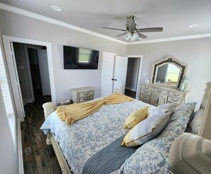 A bedroom with a bed, a ceiling fan, a TV, a dresser, and a mirror.