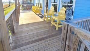 A covered wooden deck with yellow Adirondack chairs and a decorative owl statue.