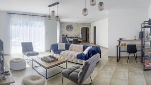Un salon moderne avec un canapé, des fauteuils, une table basse et, au fond, un coin repas.
