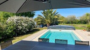 Une piscine dotée d’un patio couvert, entourée d’une végétation luxuriante et de palmiers.