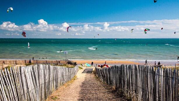 Une plage avec une clôture en bois, un sentier sablonneux et l’océan.