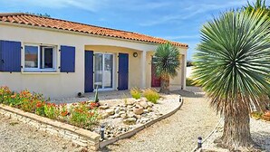 Une maison avec un toit en tuiles, une porte bleue et un jardin agrémenté de rochers et de plantes.