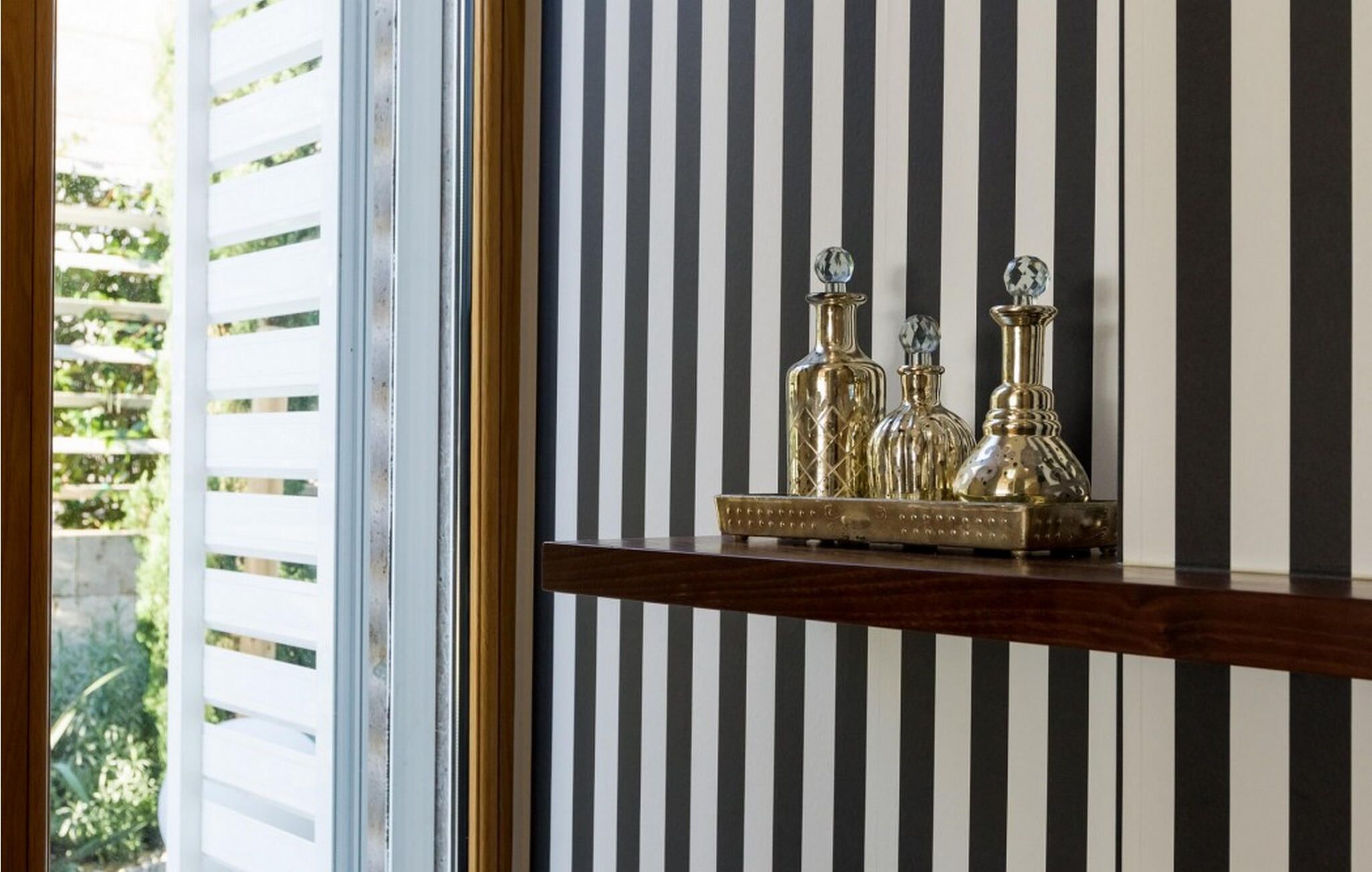 A shelf with three glass decanters against a striped wall.