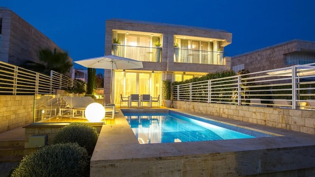 A modern two-story house with a swimming pool, outdoor seating, and a well-lit entrance.