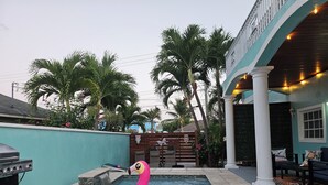 A swimming pool with a pink flamingo float, a grill, and palm trees. - Boho- Baha Retreat  Pool  7 min Beach & Airport (Nassau)
