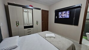 A hotel room with a bed, a wardrobe, a television mounted on the wall, and a bathroom visible through an open door. - Condomínio Frente mar pé na Área, Piscinas Naturais! Casa Térreo Aconchegante (Camaçari)