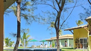 A pool area with a clear view of the pool, lounge chairs, and a building with the number 19. - Condomínio Frente mar pé na Área, Piscinas Naturais! Casa Térreo Aconchegante (Camaçari)