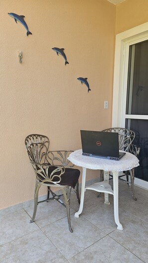 A patio area with a round table and two chairs, a laptop on the table, and three dolphin wall art pieces.