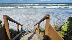 A wooden staircase leading to a beach with waves in the background. - Condomínio Frente mar pé na Área, Piscinas Naturais! Casa Térreo Aconchegante (Camaçari)