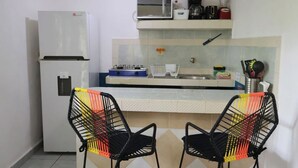 A compact kitchen with a refrigerator, microwave, stove, and a small sink. There are two chairs with a colorful backrest. - Comfy studio on downtown, 3 blocks to ocean views, calm, safe & quiet (San Miguel de Cozumel)